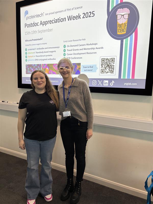 Two people standing beside a presentation about Proteintech's Postdoc Appreciation Week 2025